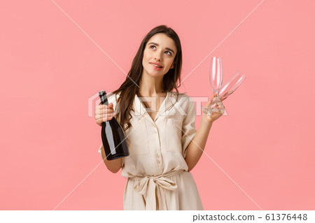Dreamy and romantic young beautiful woman planning valentines day date, standing thoughtful looking up imaging perfect wedding, holding champagne and two glasses, smiling sensual 61376448