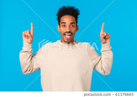 You gotta try this. Outgoing amazed and excited happy smiling african-american man loves winter holidays, attend awesome party, pointing fingers up, having fun and telling about promo, blue wall 61376665