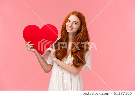 Celebration, love and relationship concept. Cute teenage girl confessing sympathy on valentines day, girlfriend with red hair in white dress asking going prom together, showing big red heart, smiling Celebration, love and relationship concept. Cute teenage girl confessing sympathy on valentines day, girlfriend with red hair in white dress asking going prom together, showing big red heart, smiling 61377190