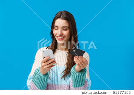 Waist-up portrait relaxed, smiling gorgeous woman in winter sweater, paying for purchase, send money to friend with app, insert billing info, credit card number at application, holding smartphone Waist-up portrait relaxed, smiling gorgeous woman in winter sweater, paying for purchase, send money to friend with app, insert billing info, credit card number at application, holding smartphone 61377193