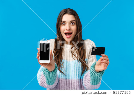 Smiling, excited and fascinated young woman talking about cool new app, banking application, deposit or cashback service, holding smartphone facing display camera, credit card, grinning amused Smiling, excited and fascinated young woman talking about cool new app, banking application, deposit or cashback service, holding smartphone facing display camera, credit card, grinning amused 61377195