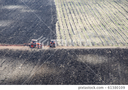 Two tractors working on burned farmland. 61380109