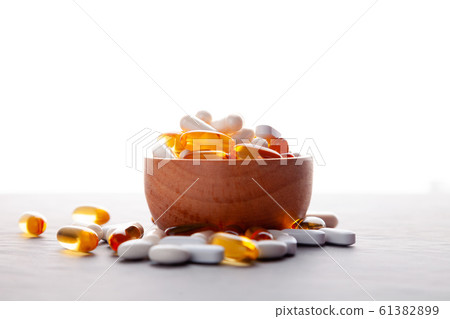 Assortment scattered pharmaceutical medicine vitamins, pills, drugs in wooden bowl on gray background. White food dietary supplement hard shell capsules filled with powder, fish oil softgel Omega 3 61382899