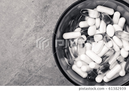Many scattered medicine vitamins, pills, drugs in bowl on gray background. White food dietary supplement hard shelled capsules fill with powder, salmon oil softgel Omega 3. Black and white photo 61382939