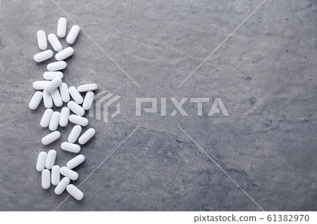 Closeup scattered white medicine vitamins, pills, drugs on gray background. White food diet supplement. Black and white photography. Top view 61382970
