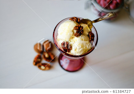 Creamy ice cream with honey and walnuts. Served in a bowl with ice cream, garnished with walnuts and honey. On the table is a jar with dried strawberries, a spoon and a walnut. Creamy ice cream with honey and walnuts. Served in a bowl with ice cream, garnished with walnuts and honey. On the table is a jar with dried strawberries, a spoon and a walnut. 61384727