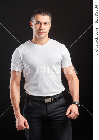 Handsome Athletic man in white blank t-shirt standing on black wall background 61385534