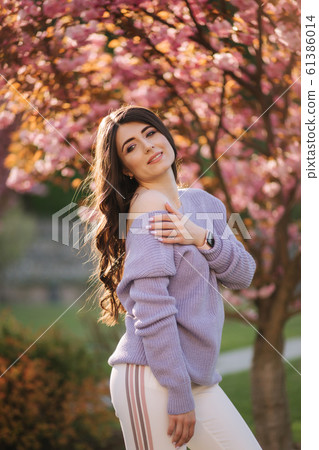 Attractive young woman in a purple sweater stand in front of sakura tree in the park 61386014