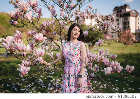 Charming girl stand by the beautiful pink magnolia tree outside. Gorgeous lady 61386102