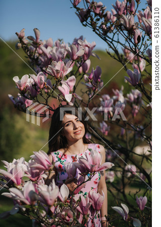 Charming girl stand by the beautiful pink magnolia tree outside. Gorgeous lady 61386110