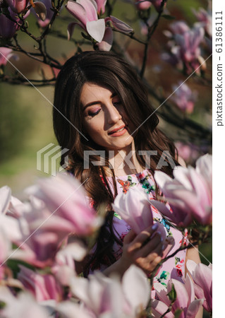 Charming girl stand by the beautiful pink magnolia tree outside. Gorgeous lady 61386111
