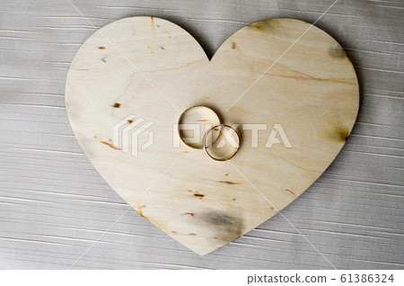 Gold wedding rings on a wooden heart.  61386324