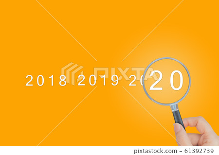 Female hand holding magnifying glass and looking at 2020 text words. 61392739
