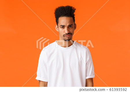 Displeased young african-american skeptical man, frowning and smirk, looking with condemn or disapproval, feeling unsure about bad idea, hesitating dont like plan, orange background 61393592