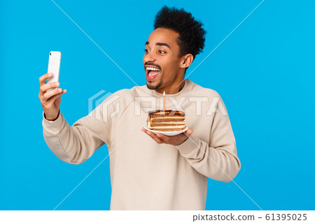 Excited happy african-american bearded hipster guy holding piece cake with birthday candle, smiling joyfully taking selfie or record video how he celebrates, making wish, standing blue background Excited happy african-american bearded hipster guy holding piece cake with birthday candle, smiling joyfully taking selfie or record video how he celebrates, making wish, standing blue background 61395025