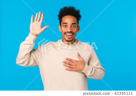Friendly happy and attractive guy introduce himself, hold palm on heart and raise one hand, make promise, telling truth, being sincere as confess love or affection, smiling standing blue background Friendly happy and attractive guy introduce himself, hold palm on heart and raise one hand, make promise, telling truth, being sincere as confess love or affection, smiling standing blue background 61395111