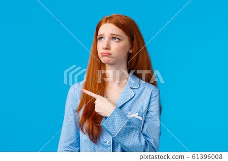 Envy and sad sulking moody redhead teenage girl in nightwear, looking and pointing upper left corner unsatisfied, jealous expression, seeing something she wants, feeling uneasy, blue background Envy and sad sulking moody redhead teenage girl in nightwear, looking and pointing upper left corner unsatisfied, jealous expression, seeing something she wants, feeling uneasy, blue background 61396008