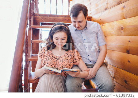 a loving couple embraces on the stairs. A man and a woman look into each other's eyes. Husband hugs pregnant wife and read a book. Valentine's day. February 14 a loving couple embraces on the stairs. A man and a woman look into each other's eyes. Husband hugs pregnant wife and read a book. Valentine's day. February 14 61397332