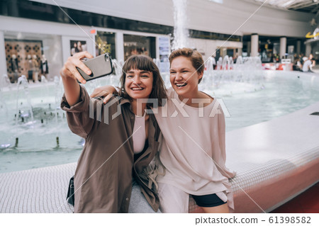Two girls take a selfie in the mall, a fountain in the background 61398582