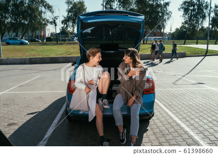 Two girls in the parking lot at the open trunk posing for the camera. Two girls in the parking lot at the open trunk posing for the camera. 61398660