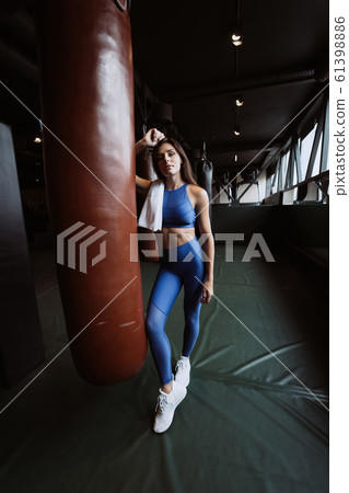 Smiling fit girl holding towel and taking rest in gym near punching bag Smiling fit girl holding towel and taking rest in gym near punching bag 61398886