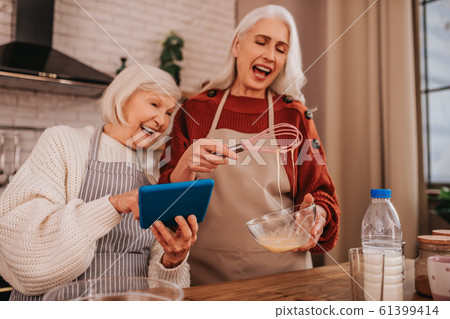 Grey-haired smiling lady in apron showing something on her smartphone Grey-haired smiling lady in apron showing something on her smartphone 61399414