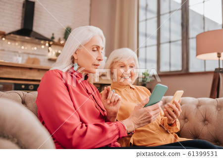 Two pleasant-looking elderly grey-haired women looking involved Two pleasant-looking elderly grey-haired women looking involved 61399531