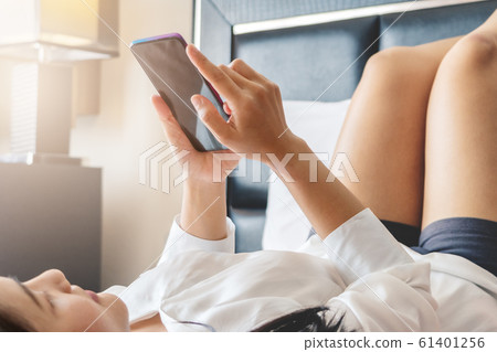 Happy woman lay on bed while surfing internet and send message on smartphone Happy woman lay on bed while surfing internet and send message on smartphone 61401256