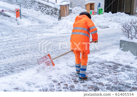 Road cleanup worker in bright orange coat clearing up snow from a street in St. Moritz Road cleanup worker in bright orange coat clearing up snow from a street in St. Moritz 61405554