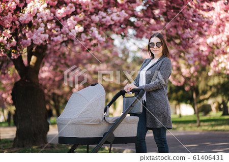 Happy mom walk with her little baby girl in stroller. Background of pink sakura tree Happy mom walk with her little baby girl in stroller. Background of pink sakura tree 61406431