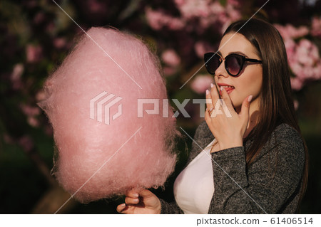 Close up portrait of attractive young girl eating cotton candy in front of pink sakura tree 61406514