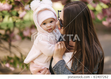 Portrait of mother and her little baby girl. Beautiful mom and cute baby. Mother hug her daughter. Baby dressed in peanch colour hat and smile 61407262