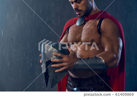 Muscular spartan looking at raindrops on helmet. Muscular spartan looking at raindrops on helmet. 61409869
