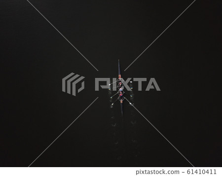 Four people rowing with an instructor in the background of black water 61410411