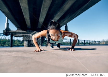 Young athletic woman doing push ups outdoors in urban city background 61411022