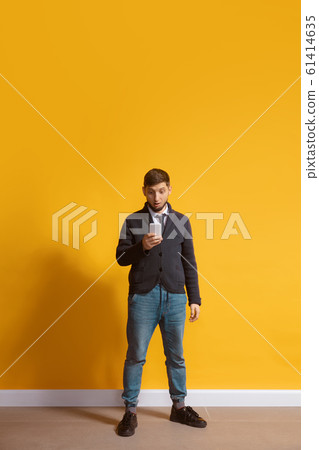 Young caucasian man using smartphone. Full body length portrait isolated over yellow background. 61414635