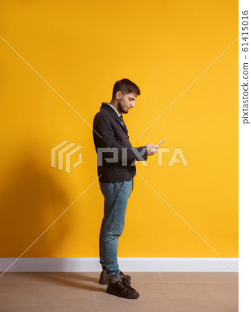 Young caucasian man using smartphone. Full body length portrait isolated over yellow background. 61415016