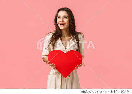 Amused and carefree good-looking european female in dress, holding valentines card, big red heart, looking left amazed and happy, smiling impressed, standing pink background joyful Amused and carefree good-looking european female in dress, holding valentines card, big red heart, looking left amazed and happy, smiling impressed, standing pink background joyful 61415059