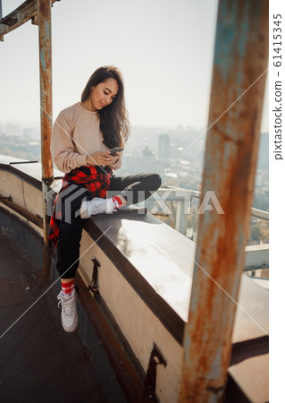 Smiling pretty girl looking on phone screen on roof Smiling pretty girl looking on phone screen on roof 61415345