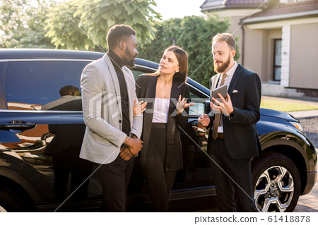 Salesman with tablet and clients, business couple, Caucasian woman and African man, standing near new car outdoors. Business people using tablet standing near black car outdoors Salesman with tablet and clients, business couple, Caucasian woman and African man, standing near new car outdoors. Business people using tablet standing near black car outdoors 61418878