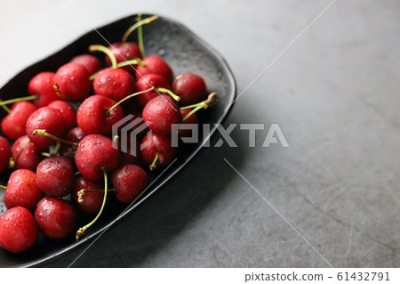 Fresh cherries covered with water droplets in a black bowl on a dark background. 61432791