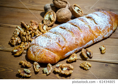 Fresh roll with walnuts and icing sugar on a wooden background. Sweet dessert with nuts on an old table. 61434805