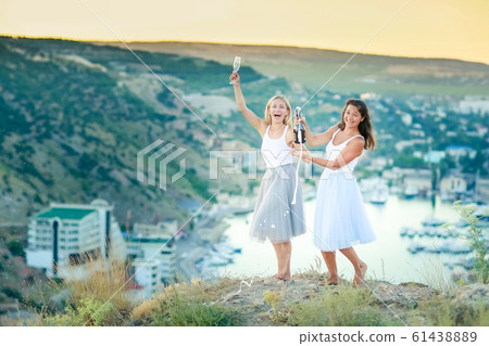 Two happy young women drinking together and having fun on top of a mountain 61438889