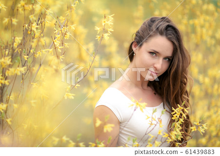 Portrait of a woman in a white dress on a background of yellow bushes with flowers Portrait of a woman in a white dress on a background of yellow bushes with flowers 61439883