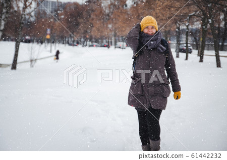 Happy young european woman in a yellow knitted hat and mittens with a backpack, laughs under the 61442232