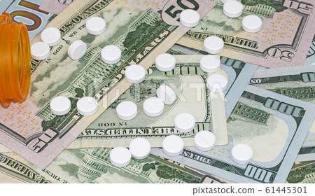 White pills spill out of container onto money White pills spill out of container onto money 61445301