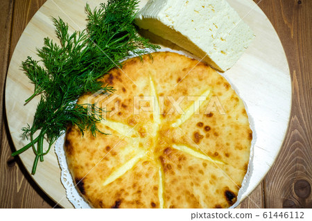 Ossetian pie with cheese and dill. A traditional dish of the Caucasian fish soup. Dough product with filling on the background of an old wooden table. The concept of tasty and healthy food. Ossetian pie with cheese and dill. A traditional dish of the Caucasian fish soup. Dough product with filling on the background of an old wooden table. The concept of tasty and healthy food. 61446112