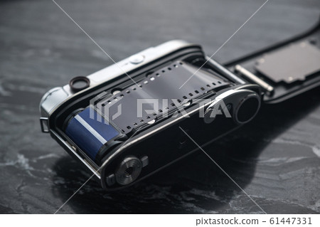 Vintage analog film camera with a lens and a charged film on a marble stone background. 61447331
