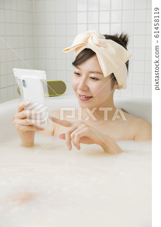 通過將智能手機放在浴室的防水盒中看智能手機的年輕女子 61458119