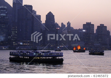 A star ferry navigating the dusk of Hong Kong Victoria Bay. In the back is the Victoria Harbor sightseeing boat "Aqualuna" 61465872